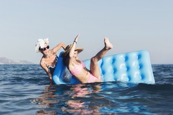 Two friends or sisters are playing, having fun and crazy game in sea water with mattress.