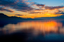Beautiful colorful sunset in autumn with silhouettes of the French Alps and fantastic orange glowing reflected colors on the Lake Geneva, Switzerland.