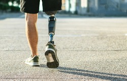 Low angle view at disabled young man with prosthetic leg walking along the street.