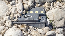 old vehicle battery buried among the stones of the river bank,pollution concept