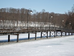 Panoramic view of the bridge over the river. Pedestrian bridge on steel supports winter day. Lanterns on the bridge in winter. The river is icebound and there is a bridge over the river.