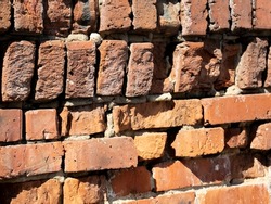 Fragment of old brickwork. Flat lay, close-up. Cracks and defects in the red brick on the wall are illuminated by bright light. Potholes and defects in red brick