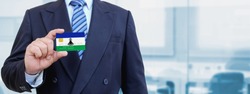 Cropped image of businessman holding plastic credit card with printed flag of Lesotho. Background blurred.