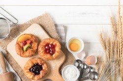 Danish bread with fruits, blueberry and cherry sauce and equipment on white wood background, bakery food