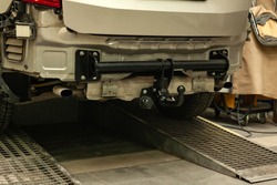 Close-up on a new black tow hitch installed on a modern car with a beige-colored bumper removed in a vehicle repair shop. The device for the transport of the trailer in the workshop.