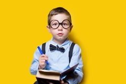 boy in glasses in a shirt and a butterfly, doing homework, on a yellow background