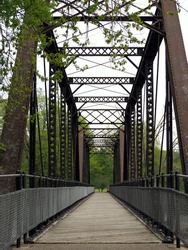 Large metal bridge with wooden footpath. Converted rails-to-trail bridge. No people. Very scenic. Taken mid-May in Portland, Michigan (USA). Vertical.