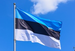 The flag of Estonia is a rectangular banner of three equal horizontal stripes of blue, black and white on a background of blue sky during the summer day.