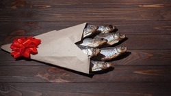 Dry fish in a paper craft bag with a red bow. Brown wood background. February 23. Gift for men. Defenders of the Fatherland Day. St. Patrick's Day. Copyspace. Selective focus.