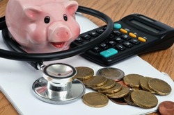 Healthcare cost concept with piggy bank, stethoscope, calculator and euro coins lying on spiral notebook