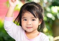 A headshot portrait of a cheerful baby Asian woman, a cute toddler little girl with adorable bangs hair, a child wearing a blue sweater smiling and looking to the camera.