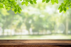 Wooden table top with green natural view of green leaves in garden and sunlight with bokeh in background.