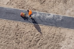 New road construction worker laying asphalt surface on walkway work. Sidewalk construction asphalt work road tarmac. Hot asphalt paving road construction site work man vibratory plate compactor rammer