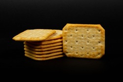 Stacked salty crackers with one salty cracker on the side on a black background