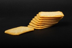 Stacked salty crackers with one salty cracker on the side on a black background
