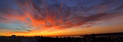 Panorama of dawn fire in the sky over a small seaside city. Golden red clouds just before the sunrise. Scenic landscape at sunrise. Beauty in nature.