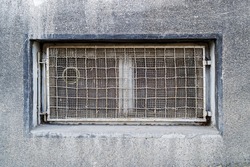 Rectangular basement or cellar window is tightened with wire metal mesh and grille. Technical floor window in the wall of an old gray building. Front view.