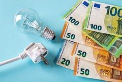 Electric plug, light bulb and euro money banknotes over blue background. Increasing of electricity cost for residential and business users, expensive energy bill and rise in electricity prices concept