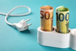 Euro money paper banknotes plugged into a white power strip over blue bacground. Increasing cost of electricity for business users and residential customers. Rise in electricity prices concept. 