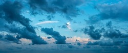 Blue stormy clouds blown by the strong wind across the sky at evening. Dramatic sky with torn dark clouds low over the horizon. Overcast skyscape panorama at blue hour. Wide windy weather cloudscape.