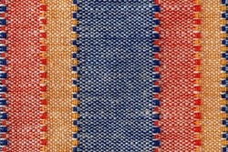 Macro texture of plain weave fabric. Striped cloth background of red, blue, orange and white colors. Textile canvas surface close-up. Design element of colorful woven fabric. Weft and warp. Top view.