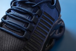 Lacing of new textile mesh sneakers on a blue background. Laced up sport shoe of black blue colors macro. Modern grooved men sneakers for fitness and active lifestyle. Sport shoes concept. Close-up.