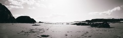 A black and white pano photo of the beach sand and rocks on the horizon in Ireland on Annestown Beach