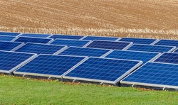 An array of photovoltaic solar panels in agriccultural setting, providing green energy. Located on a grassed field, with harrowed stubble field background. Landscape image with space for text. UK.