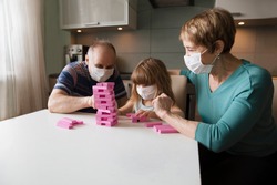 grandparents with granddaughter wearing medical face mask playing  board game together at home. quarantine. health concept. Corona Virus. 