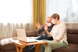Seniors couple  grandmother and grandfather wearing medical face mask and using laptop Communicate with grandchildren online at home. quarantine. standing in home. chelter in place.