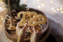women's hands hold numbers 2022 against the background of Christmas decor

