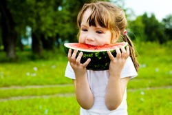 cute little girl eating  watermelon on the grass in summertime
