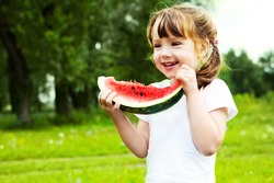 cute little girl eating  watermelon on the grass in summertime