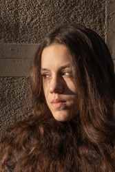 Close up portrait of young attractive girl with grey eyes and dark open hair. Girl with serious facial expressions looking away from the camera. Outdoor shot. Details of girl's face.
