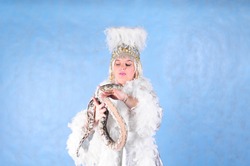 Animator a woman in the Studio on a blue background in a white dress and a fluffy headdress in the Studio with a snake in her arms