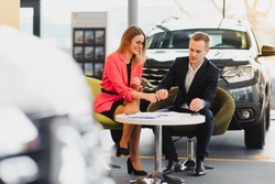 Car dealership sales person at work concept. Portrait of young sales representative wearing formal wear suit, showing vehicles at automobile exhibit center. Close up, copy space, background.