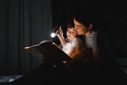 happy family mother and child son reading a book with a flashlight. Family before going to bed mother reads to her child son book near a flashlight in the evening.