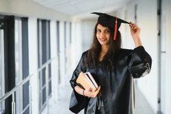 Happy Indian university student in graduation gown and cap holding diploma certificate.