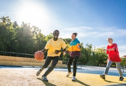 Multicultural group of young friends bonding outdoors and having fun - Stylish cool teens gathering at basketball court, friends playing basketball outdoors