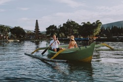 Young beautiful couple paddling on a wooden boat at Pura Ulun Danu Bratan, Bali - Tourists exploring Bali