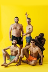 group of multiethnic men posing for a male edition body positive beauty set. guys with different age, and body wearing trunks swimwear ready to go at the beach