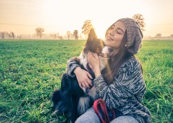 Young beautiful girl stroking her dog in a park at sunset - Asian woman playing with her dog