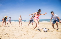 Group of multiethnic friends playing soccer on the beach - Football match on the sand on summertime - Tourists having fun on vacation with beach games
