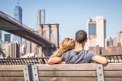 Couple in love sitting on a bench and staring at Brooklyn Bridge and Manhattan skyline - Romantic date
