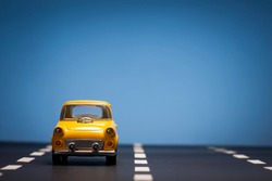 Front view of a Yellow toy car on a blue background and on an asphalt road.