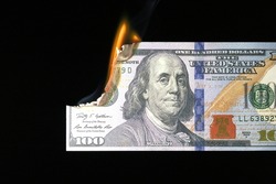Close up shot of a 100 dollar banknote burning on a black background.