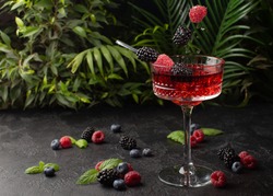 Fresh berries cocktail with raspberry,blackberry,mint and ice with tropical plants on background.Shot of drink in freeze motion,flying drops and berries.Summer cold drink and cocktail.