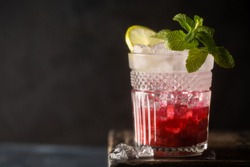Refreshing cocktail with berry syrup or liqueur,tonic,crushed ice,fresh mint and lime on dark background.Close up of refreshing drink.