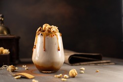 Sweet Milkshake with caramel syrup,cream liqueur,caramel popcorn and chocolate powder on brown background with vintage,manual coffee grinder.