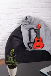 A red ukulele lies on a black bean bag, next to a black table. Learning to play a musical instrument online. Online learning concept